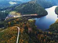 Malownicze jezioro Lubachowskie otoczone lasami, z krętą drogą wijącą się po zboczu i zabudowaniami nad brzegiem.