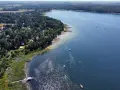 Malownicze jeziora w pomorskim, z piaszczystą plażą, lasem i domkami letniskowymi. Na wodzie żaglówki i kąpielowicze.
