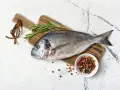 Świeża dorada, kuzynka leszcza, na drewnianej desce z rozmarynem i kolorowym pieprzem.