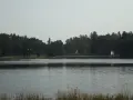 Spokojne jezioro zmarłe otoczone gęstym lasem. Na brzegu widać kilka domków.