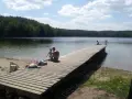 Rodzina odpoczywa nad jeziorem Zawiad. Drewniane molo, piasek i las tworzą idealne miejsce na letni relaks.