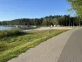 Słoneczny dzień nad jeziorem Firlejowskim. Woda, piaszczysta plaża z dmuchanymi atrakcjami i ścieżka rowerowa.