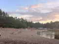 Plaża nad jeziorem Jelcz Laskowice tętni życiem. Ludzie odpoczywają na piasku, kąpią się w wodzie, a dzieci bawią się na dmuchanych zjeżdżalniach.