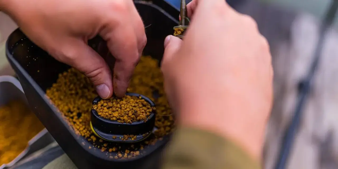 Ręce przygotowują zanętę, nabierając pellet z pojemnika. To kluczowy etap, by dowiedzieć się, jak wysuszyć pellet do wędkowania.