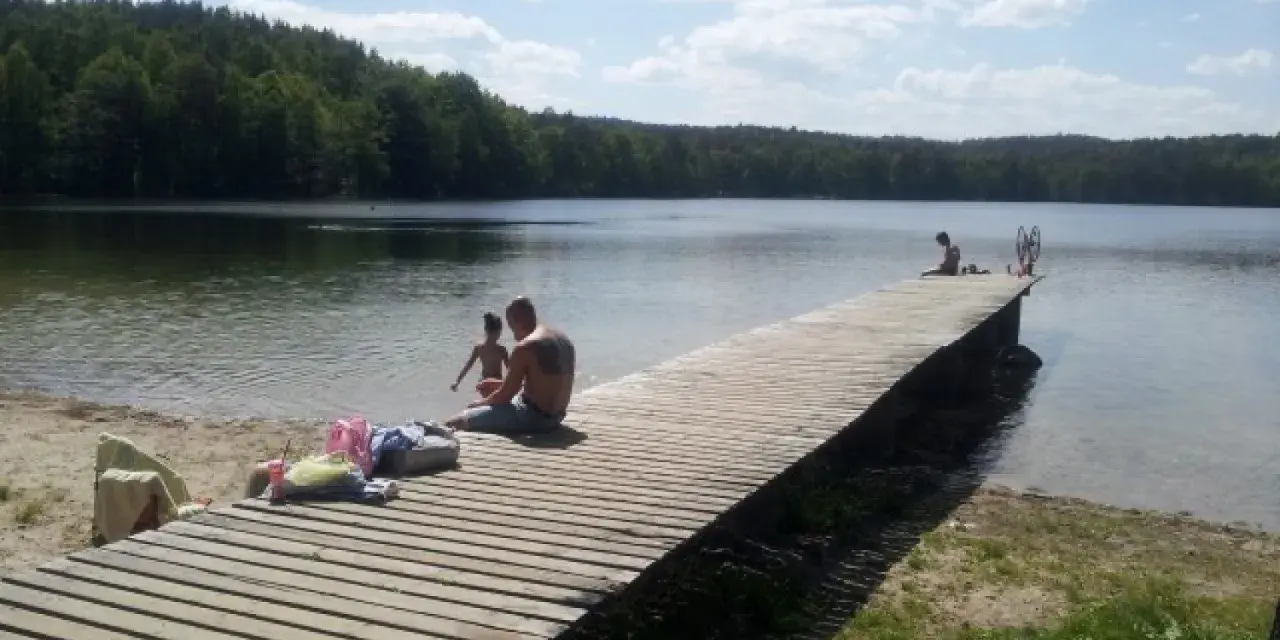 Rodzina odpoczywa nad jeziorem Zawiad. Drewniane molo, piasek i las tworzą idealne miejsce na letni relaks.