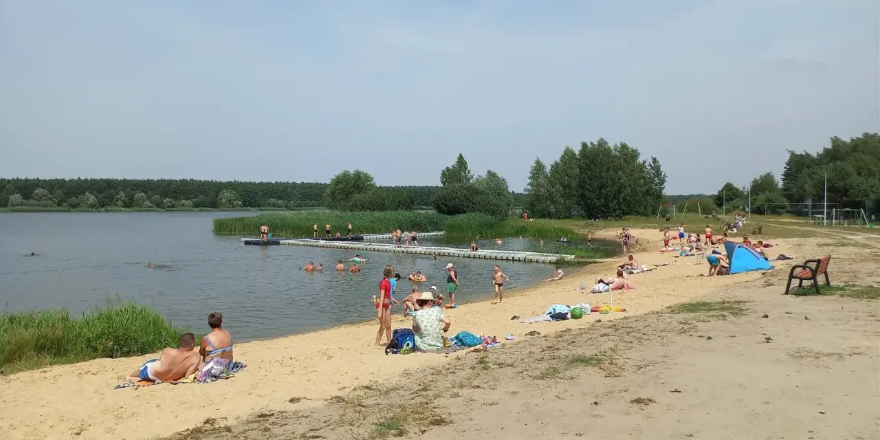 Słoneczny dzień nad zalewem Murowaniec. Ludzie kąpią się, opalają na plaży i odpoczywają.
