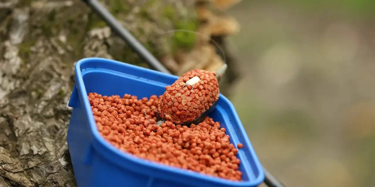 Niebieskie pudełko z pomarańczowym pelletem, idealne do nauki, jak samemu zrobić pellet na ryby.
