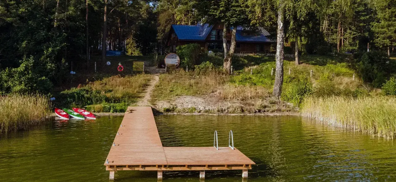 Drewniany pomost nad jeziorem Zagnanie, obok trzy kajaki. W tle dom wśród drzew.