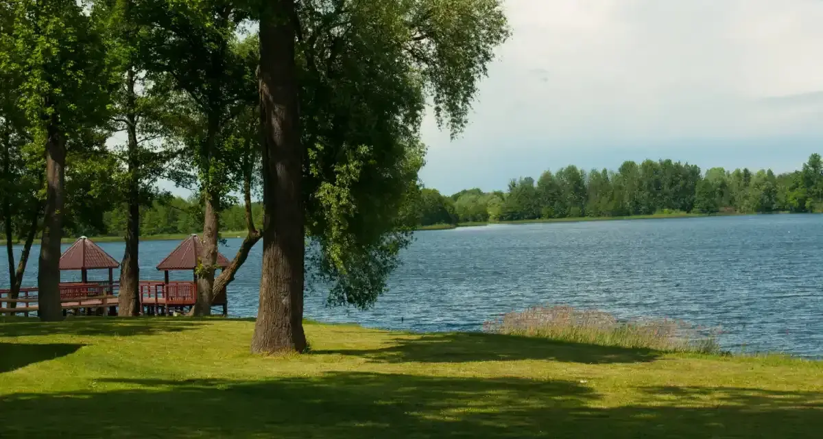 Malownicze jezioro Szczutowskie z altanami na brzegu, otoczone zielenią.