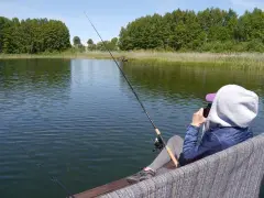 Osoba łowi ryby na spokojnym jeziorze. W tle las i trzciny. Czyżby to czas na relaks i zapomnienie o wszelkich **wody polskie opłaty**?