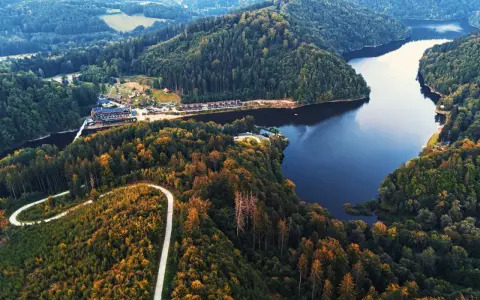 Malownicze jezioro Lubachowskie otoczone lasami, z krętą drogą wijącą się po zboczu i zabudowaniami nad brzegiem.