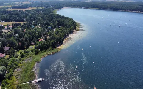 Malownicze jeziora w pomorskim, z piaszczystą plażą, lasem i domkami letniskowymi. Na wodzie żaglówki i kąpielowicze.