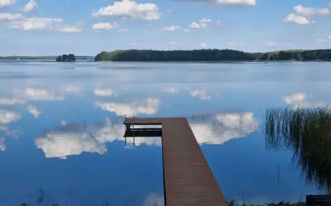 Drewniane molo prowadzi do spokojnego jeziora nisko, gdzie błękitne niebo z białymi chmurami odbija się w tafli wody.