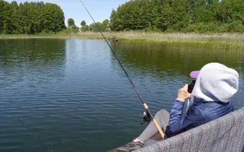 Osoba łowi ryby na spokojnym jeziorze. W tle las i trzciny. Czyżby to czas na relaks i zapomnienie o wszelkich **wody polskie opłaty**?