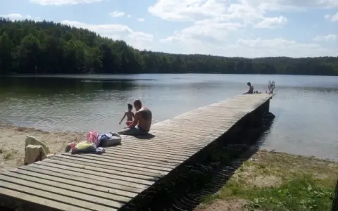 Rodzina odpoczywa nad jeziorem Zawiad. Drewniane molo, piasek i las tworzą idealne miejsce na letni relaks.