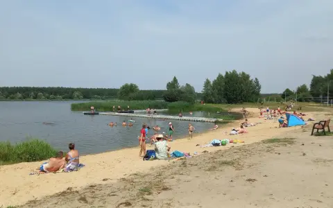 Słoneczny dzień nad zalewem Murowaniec. Ludzie kąpią się, opalają na plaży i odpoczywają.