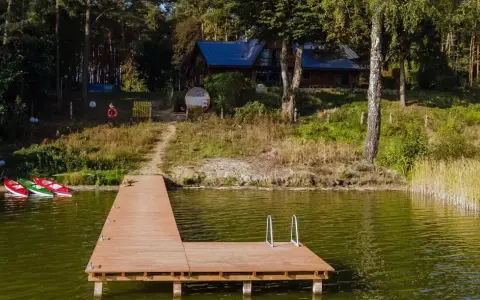 Drewniany pomost nad jeziorem Zagnanie, obok trzy kajaki. W tle dom wśród drzew.