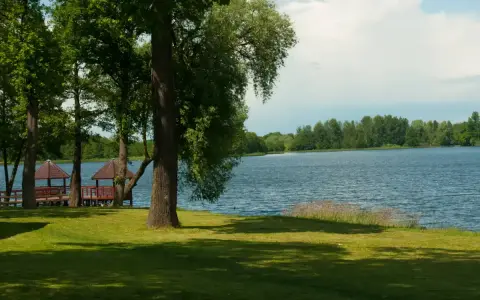 Malownicze jezioro Szczutowskie z altanami na brzegu, otoczone zielenią.