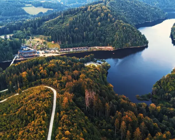 Malownicze jezioro Lubachowskie otoczone lasami, z krętą drogą wijącą się po zboczu i zabudowaniami nad brzegiem.