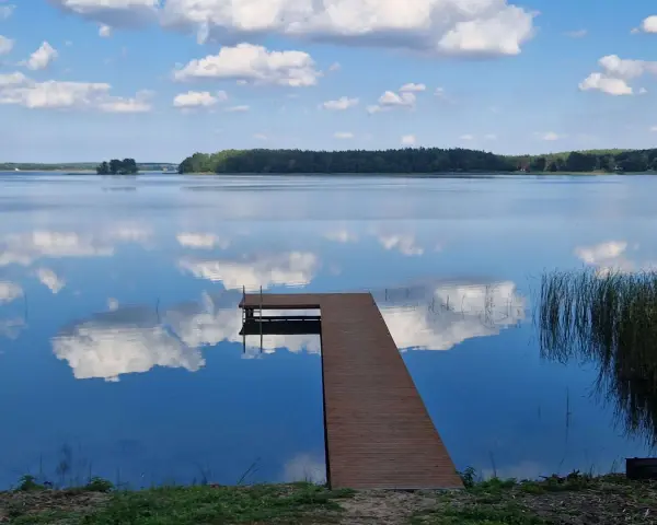 Drewniane molo prowadzi do spokojnego jeziora nisko, gdzie błękitne niebo z białymi chmurami odbija się w tafli wody.