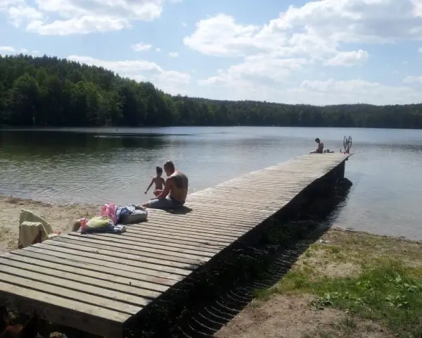Rodzina odpoczywa nad jeziorem Zawiad. Drewniane molo, piasek i las tworzą idealne miejsce na letni relaks.
