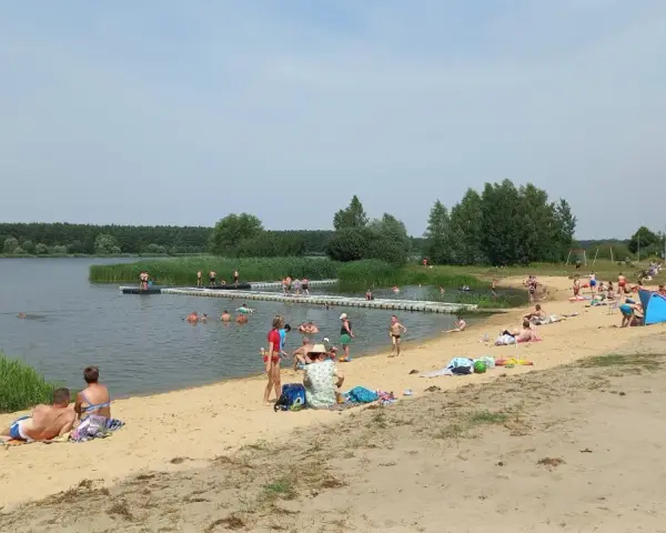 Słoneczny dzień nad zalewem Murowaniec. Ludzie kąpią się, opalają na plaży i odpoczywają.