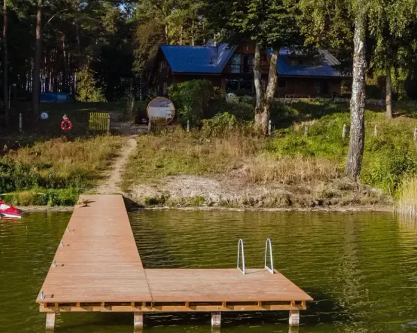 Drewniany pomost nad jeziorem Zagnanie, obok trzy kajaki. W tle dom wśród drzew.
