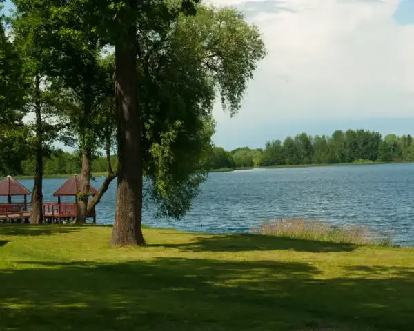 Malownicze jezioro Szczutowskie z altanami na brzegu, otoczone zielenią.