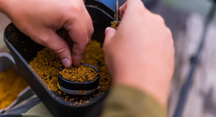 Ręce przygotowują zanętę, nabierając pellet z pojemnika. To kluczowy etap, by dowiedzieć się, jak wysuszyć pellet do wędkowania.