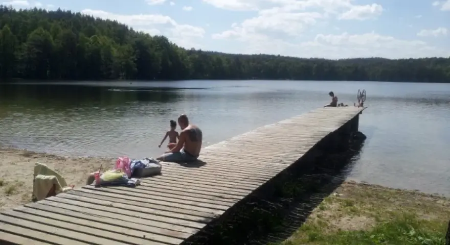 Rodzina odpoczywa nad jeziorem Zawiad. Drewniane molo, piasek i las tworzą idealne miejsce na letni relaks.