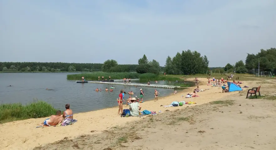 Słoneczny dzień nad zalewem Murowaniec. Ludzie kąpią się, opalają na plaży i odpoczywają.