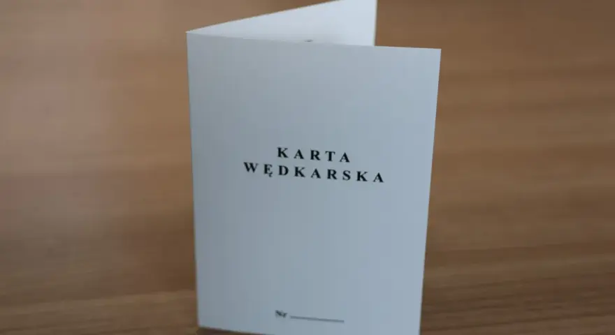 Oto jak wygląda karta wędkarska: biała, złożona kartka z napisem "KARTA WĘDKARSKA" i miejscem na numer.