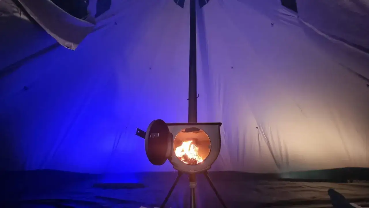 Piec w namiocie, płomienie tańczą, oświetlając wnętrze. To sposób, jak ogrzać namiot zimową nocą.