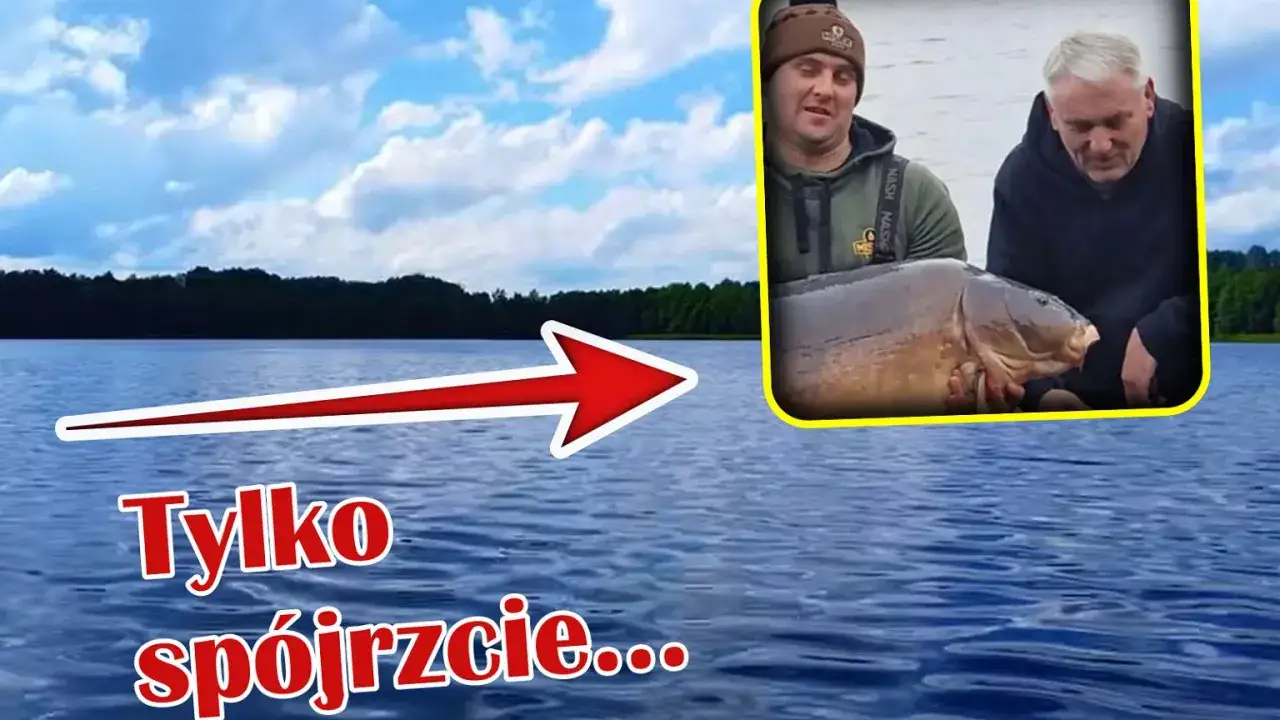 Dwóch wędkarzy prezentuje swojego wielkiego karpia złowionego na spokojnym jeziorze.
