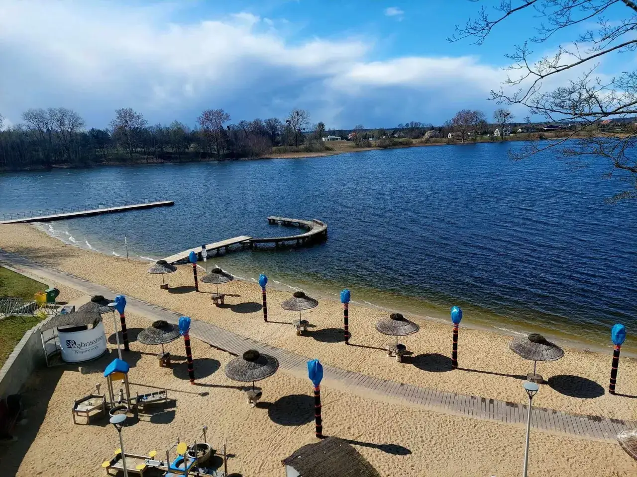 Plaża nad jeziorem zamkowym z molo, parasolami i placem zabaw.